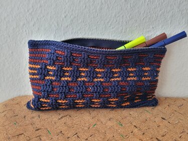Kleines gehäkeltes Etui in Dunkelblau mit orange-braunen Streifen, geöffnet und mit Stiften gefüllt