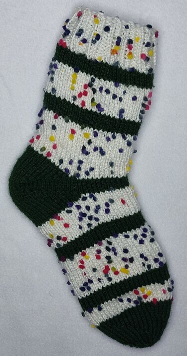 Gestrickte Socke weiß mit bunten Noppen und dunkelgrünen Streifen