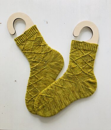 Zwei gelbgrüne, handgestrickte Socken mit erhabenem Rautenmuster auf Sockenbrettchen