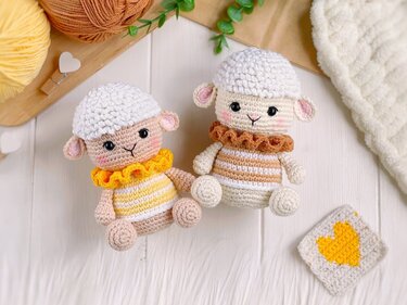 Two crocheted amigurumi lamb dolls with white caps, striped bodies, and yellow and brown ruffled collars on a light wooden background