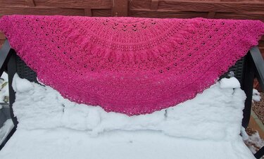 Fuchsiafarbenes halbrundes Häkeltuch über schneebedeckter Bank, kontrastreicher Hintergrund