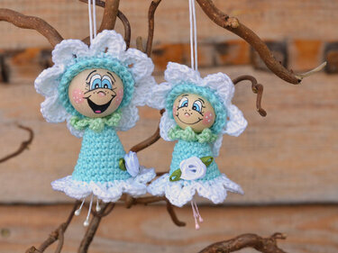 Zwei schnell gehäkelte Blumenanhänger in Pastell mit bemalten Holzperlenköpfen, aufgehängt an dünnen Bändern