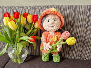 Gehäkelte Amigurumi-Puppe im orangefarbenen Outfit mit Häkeltulpen neben einer Vase mit Tulpen