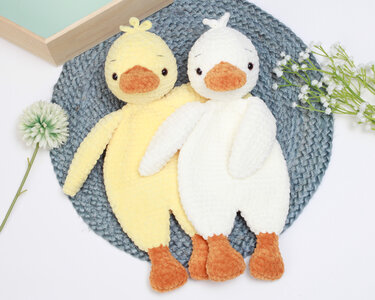 Yellow and white crocheted duckling plush toys on a blue woven mat.
