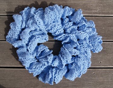 Hellblauer gehäkelter Schal mit Rüschen, liegend auf Holzdielen