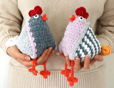 Two crochet amigurumi hens in pastel blue and lavender held in hands
