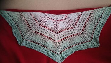Halbrund gehäkeltes Tuch in Pastellgrün mit Lochreihen und Herzmotiven auf rotem Hintergrund