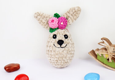 Egg-shaped crocheted bunny with stitched face and pink flower embellishments