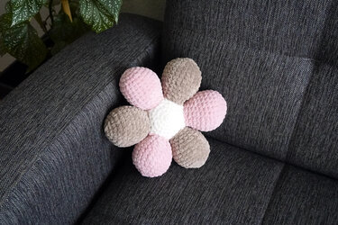 Gehäkeltes blütenförmiges Kissen in Rosa, Beige und Weiß auf dunkelgrauem Sofa.