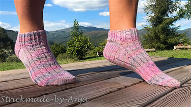 Feet wearing pink speckled knitted ankle socks standing on a wooden deck with mountains in the background