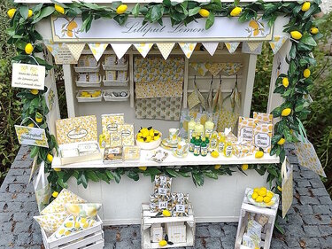 Miniatur-Zitronenstand mit Zitronengirlande, Wimpelkette, kleinen Fläschchen, Kisten und Papierverpackungen im Zitronen-Design.