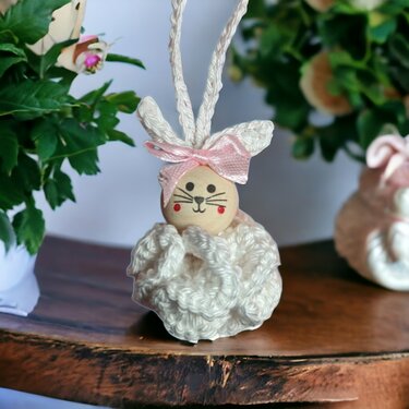 Gehäkelter Osterhase in Cremeweiß mit Holzkopf, aufgemaltem Gesicht und rosa Schleife als Anhänger.