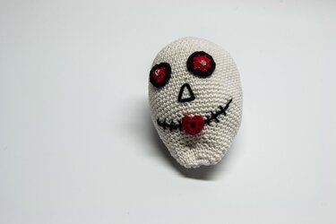 Beigefarbener gehäkelter Totenkopf mit schwarzen Augenringen und herzförmigem roten Mund