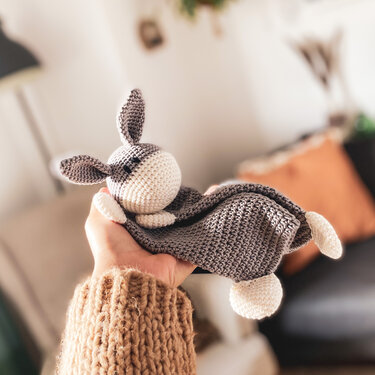 Hand holding gray and cream crocheted bunny lovey with floppy ears and small blanket