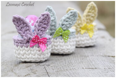 Drei gehäkelte Osterkörbchen mit Hasenohren und gepunkteten Schleifen auf Holz