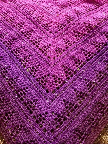 Nahaufnahme der Musterstruktur eines gehäkelten Dreieckstuchs mit V‑Reihen, Lochmustern und Perlen in Pink‑Violett