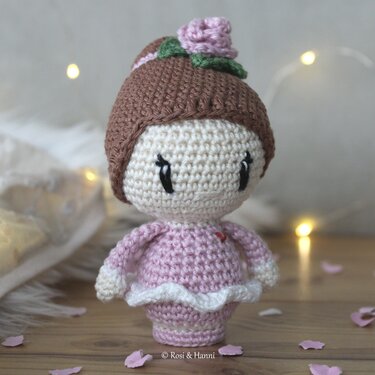 Gehäkelte Amigurumi-Ballerina in rosa Kleid mit Dutt und Rosenverzierung auf Holzuntergrund