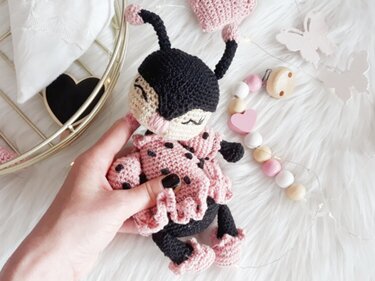 Hand hält gehäkelte Amigurumi-Puppe mit rosa Rüschenkleid, schwarzen Punkten und Antennen
