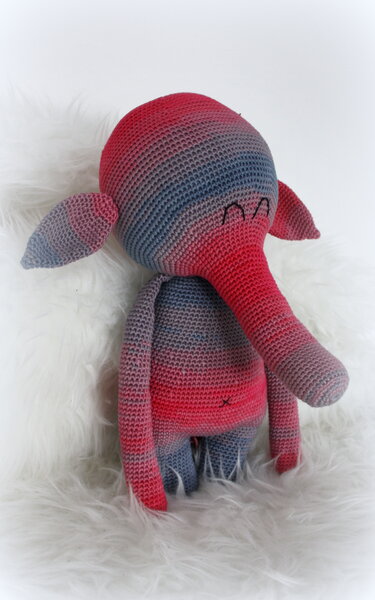 Gehäkelter Amigurumi-Elefant in rot-blau-grauem Verlaufsgarn auf flauschigem Hintergrund