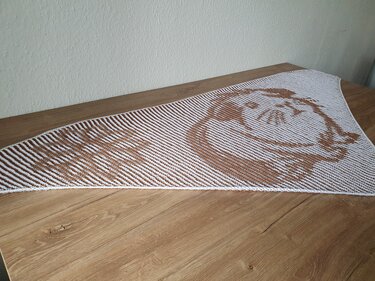 White and brown triangular knitted shawl with a stylized cat face motif laid flat.