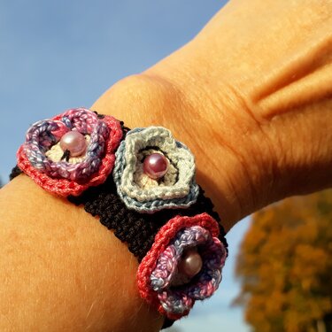 Handgelenk mit schwarzem gehäkeltem Armband und drei pastellfarbenen Häkelblüten mit Perlen
