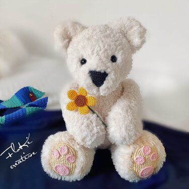 Detailansicht eines cremefarbenen gehäkelten Teddybären mit sichtbaren Pfotenapplikationen und gelber gehäkelter Blume