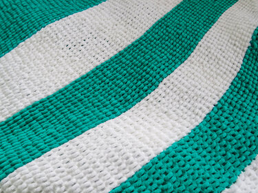 Nahaufnahme einer gestrickten Decke mit breiten weißen und türkisen Streifen und voluminöser Maschenstruktur