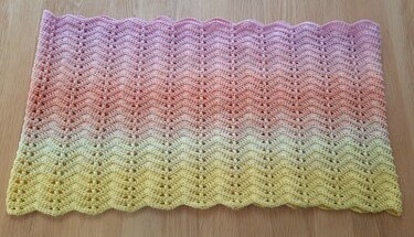 Gehäkelter Loop in pastelligen Gelb- und Rosatönen mit offenem Zickzackmuster, flach ausgelegt