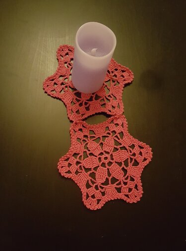 Zwei rosa gehäkelte sternförmige Deckchen auf dunklem Tisch, eines mit hellvioletter Kerze.
