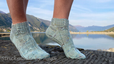 Hellblaue gestrickte Knöchelsocken mit Zopfmuster am Seeufer
