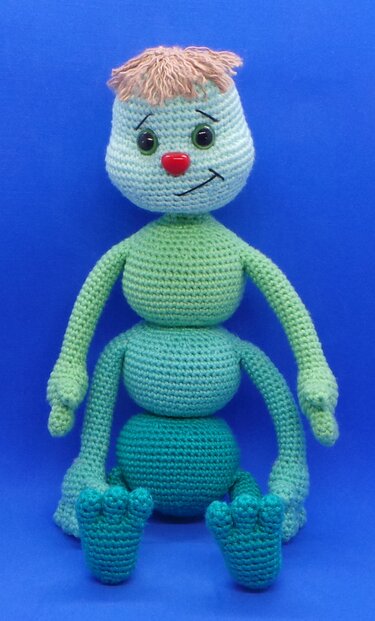 Gehäkelte Amigurumi-Raupe mit drei Kugelsegmenten, langen Armen und roter Nase vor blauem Hintergrund