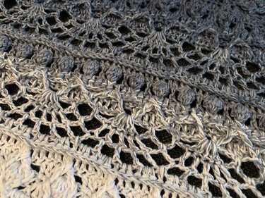 Close-up of a grey ombré crochet triangle shawl with lace mesh, shell motifs and bobble stitch row