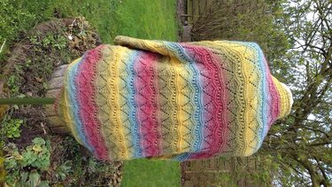 Mehrfarbiger gestrickter Seelenwärmer mit Kapuze, welliges Ajourmuster und horizontale Farbstreifen in Gelb, Rosa, Blau und Grün