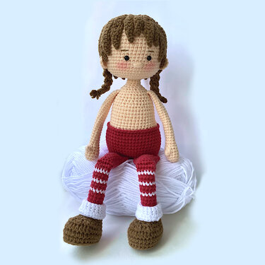 crocheted amigurumi doll with brown braided hair and red-and-white striped legs sitting on a skein of white yarn