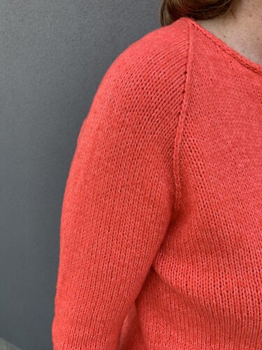 Detailaufnahme der Raglannaht und Maschenstruktur an der Schulter eines korallfarbenen Pullovers