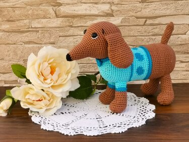 Brown crocheted dachshund amigurumi in a turquoise polka-dot sweater on a white doily