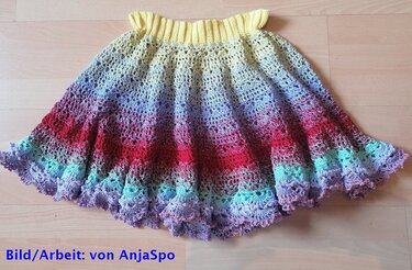 Gehäkelter Kinderrock mit Regenbogen-Farbverlauf und Rüschensaum auf Holzboden