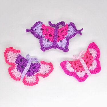 Drei gehäkelte Schmetterlinge in Pink- und Lilatönen auf weißem Hintergrund