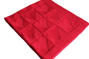 Rote gestrickte Babydecke mit quadratischen Herzmotiven