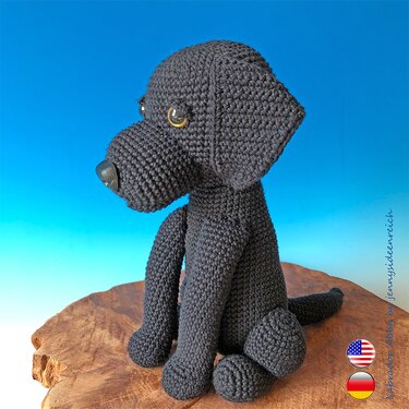 Gehäkelter schwarzer Amigurumi-Hund sitzend auf Holzuntergrund