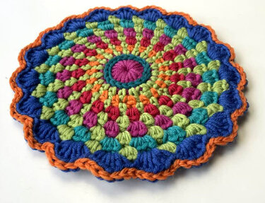 Rundes gehäkeltes Mandala in Blau, Grün, Pink und Orange mit Muschelkante
