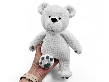 Weißer gehäkelter Amigurumi-Eisbär mit grauen Tatzenpads, Hand als Größenvergleich