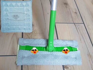 Hellblauer gestrickter Wischmoppbezug auf einem grünen Wischmopp und ein passendes quadratisches Putztuch auf Holzboden.