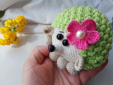 Hand holding a crocheted amigurumi hedgehog with a textured green back and a pink flower