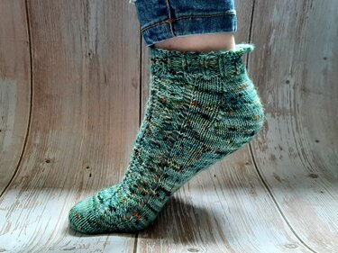 Handgestrickte türkise Kurzsocke mit Lochmuster, getragen auf einem Holzboden.