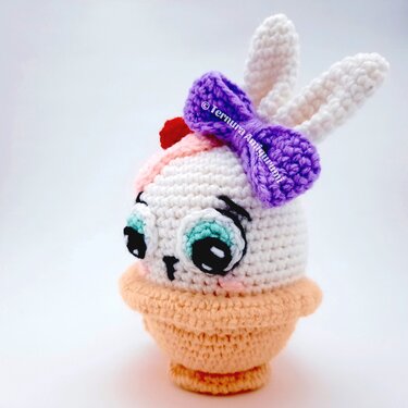 crocheted pastel amigurumi rabbit with purple bow sitting in a peach cup