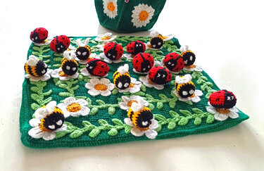Gehäkelte grüne Spielmatte mit Marienkäfern, Bienen und Gänseblümchen.