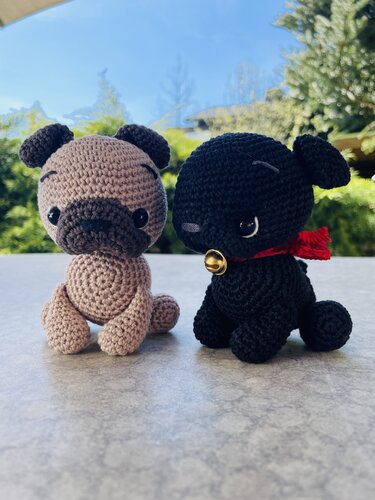 Zwei sitzende gehäkelte Hunde, beige und schwarz, schwarzer mit rotem Halstuch und kleinem Glöckchen