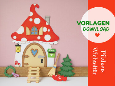 Rotes Pilzhaus mit weißen Punkten, braune Wichteltür mit Herzfenster, kleine Leiter, Briefkasten, Besen, Holzschuhe, Tannenbaum und Kranz vor rosa Hintergrund.