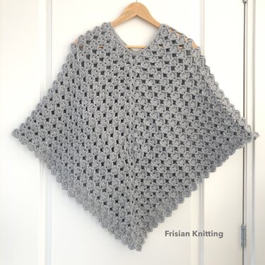Grey crocheted V-neck poncho on wooden hanger with diamond shape and scalloped edge